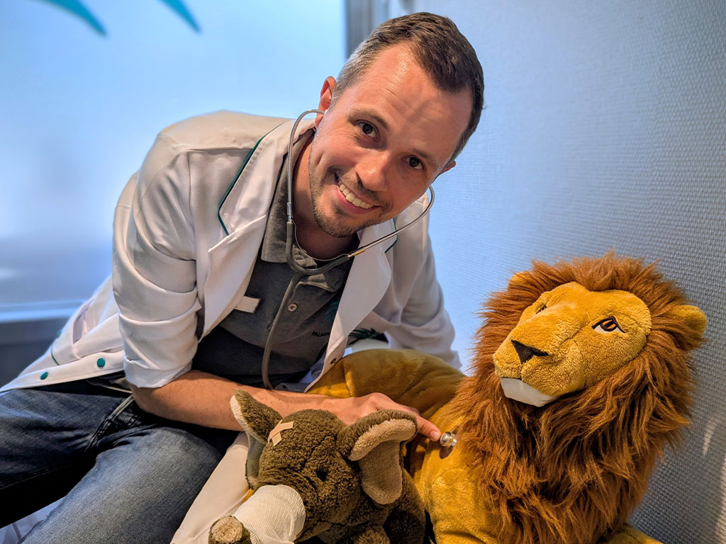 Ein Apotheker untersucht mit einem Stethoskop spielerisch einen großen Plüschlöwen in der Apotheke