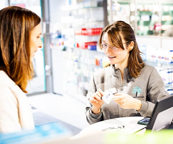 Mitarbeiterin der Palmen Apotheke in Ottobrunn berät eine Kundin persönlich am HV Tisch.